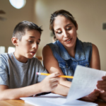 mother teaching her don to read while holding the paper.
